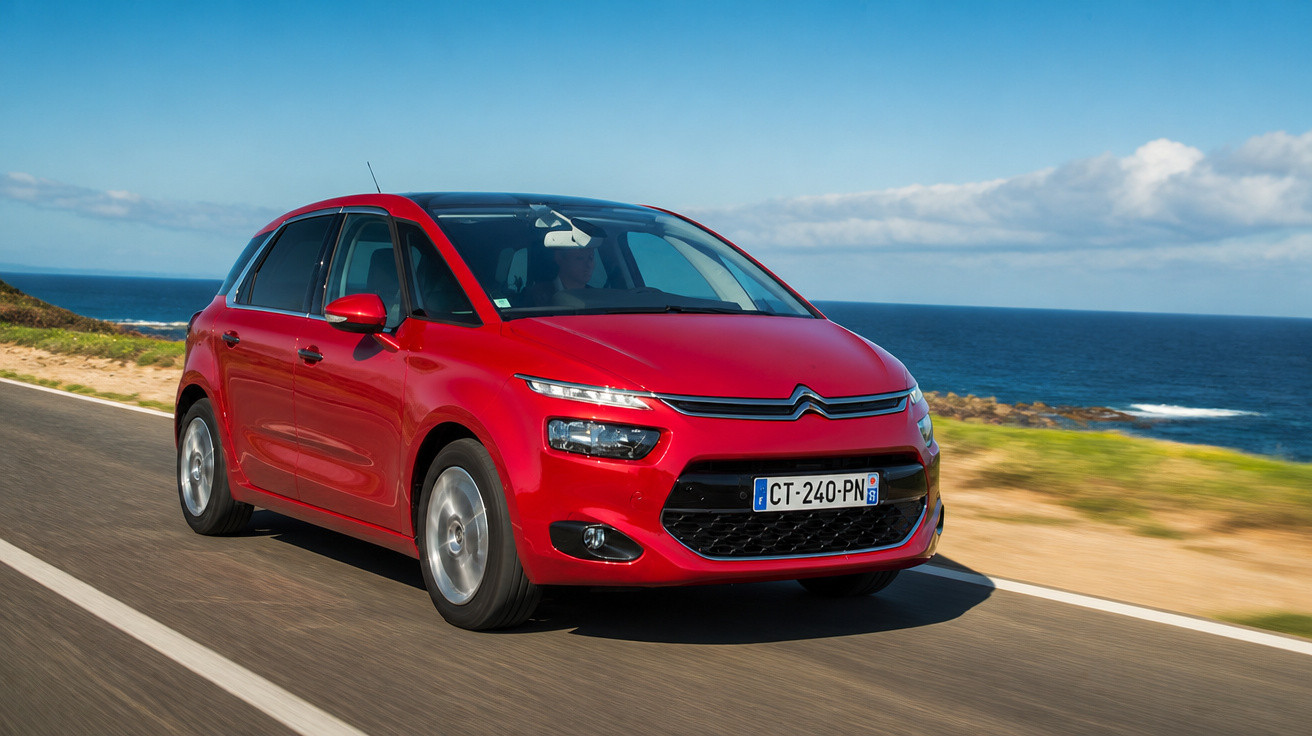 Carro vermelho Citroën em estrada costeira com mar e céu azul ao fundo em dia ensolarado.